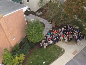 An aerial shot of a group of people standing outside of a building looking up at the camera